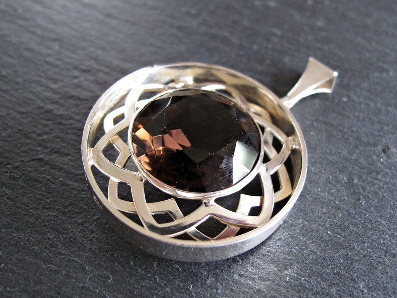 May include: A silver pendant featuring a brown gemstone set within a Celtic knot design.