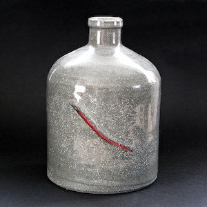 以下が含まれることがあります： 丸みを帯びたボディと細い首を持つ、グレーの斑点のあるセラミックボトル。ボトルの前面には細い赤い線が描かれています。ボトルは黒い背景に置かれています。