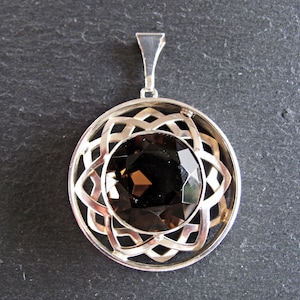 May include: A silver pendant featuring a brown gemstone set within a circular, intricate design.