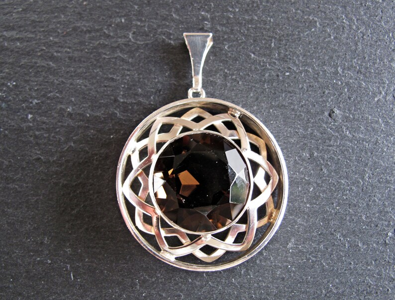 May include: A silver pendant featuring a brown gemstone set within a circular, intricate design.