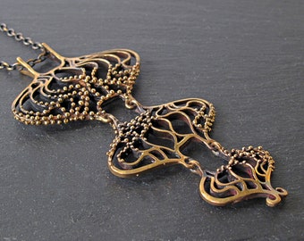 May include: A delicate bronze necklace with a detailed, intricate design. The pendant features a layered, openwork pattern with small, round beads. The necklace is suspended from a black chain.