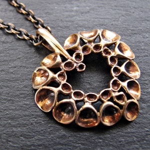 May include: A bronze pendant necklace with a circular design featuring a repeating pattern of small, rounded shapes. The pendant is attached to a black chain.