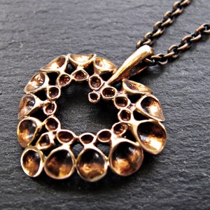 May include: A bronze pendant necklace with a circular design featuring a repeating pattern of small, rounded shapes. The pendant is attached to a silver chain.