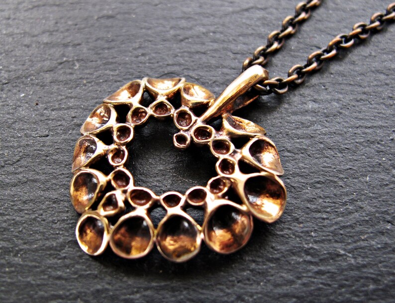 May include: A bronze pendant necklace with a circular design featuring a repeating pattern of small, rounded shapes. The pendant is attached to a silver chain.