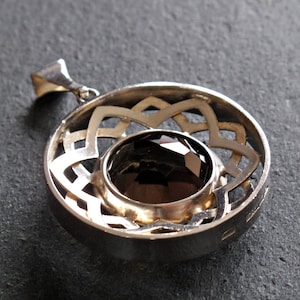 May include: Silver pendant featuring a dark brown gemstone set within a circular, openwork design.
