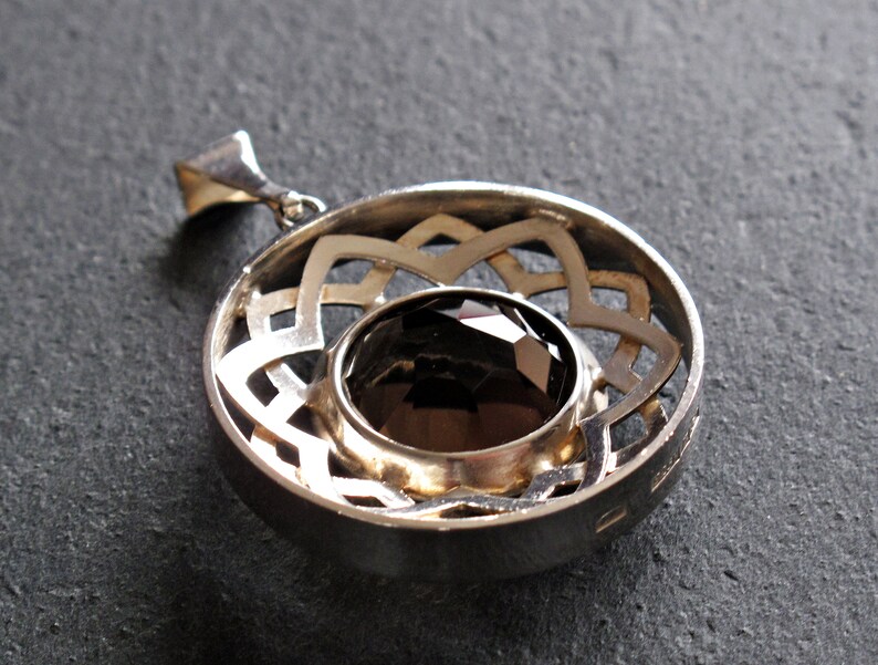 May include: Silver pendant featuring a dark brown gemstone set within a circular, openwork design.
