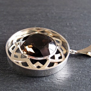 May include: A silver pendant featuring a round, faceted smoky quartz gemstone set within a Celtic knot design.