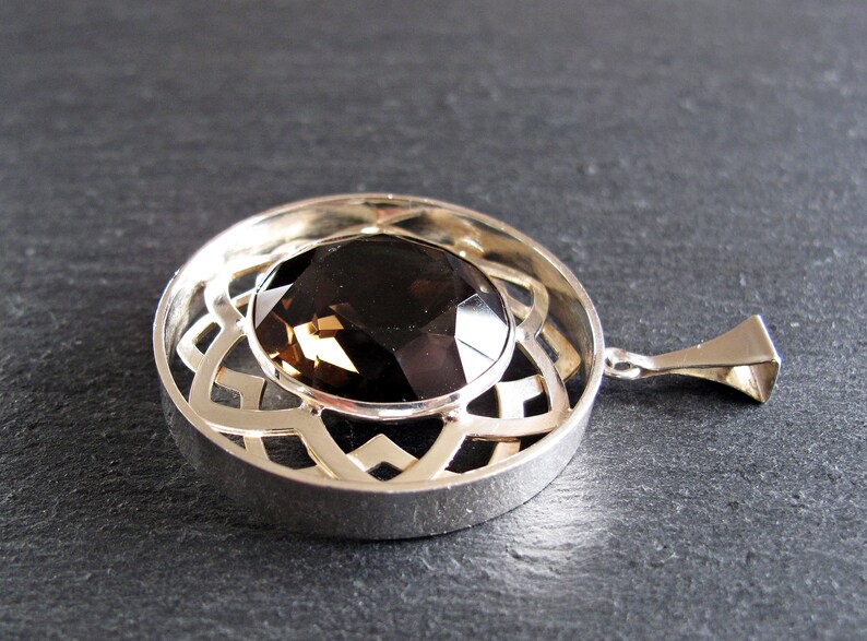 May include: A silver pendant featuring a round, faceted smoky quartz gemstone set within a Celtic knot design.