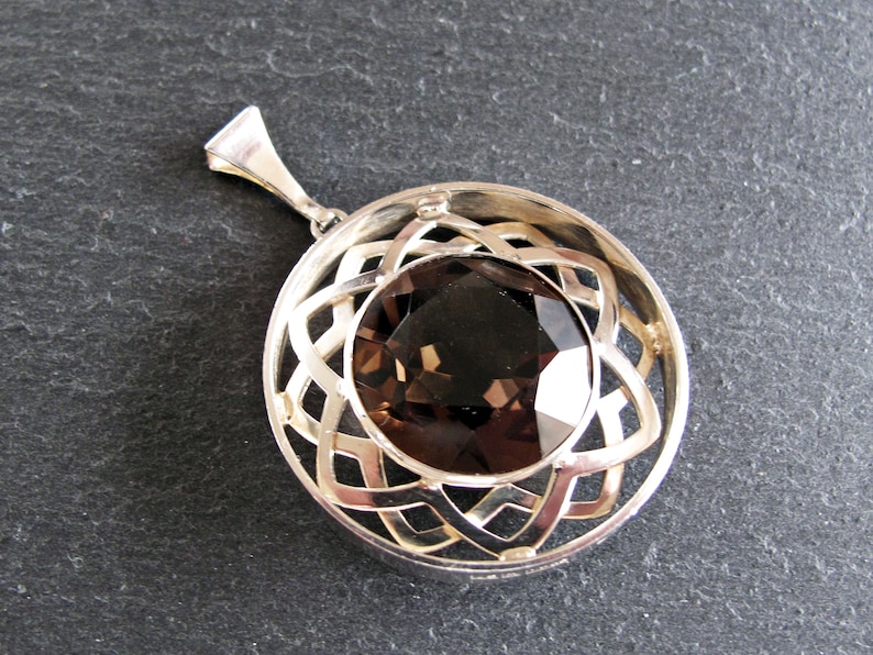 May include: A silver pendant featuring a brown gemstone set within a Celtic knot design.