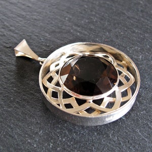 May include: A silver pendant featuring a round, faceted, dark brown gemstone set within a circular, openwork design.