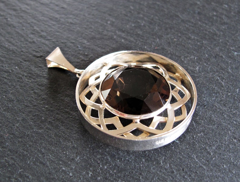 May include: A silver pendant featuring a round, faceted, dark brown gemstone set within a circular, openwork design.
