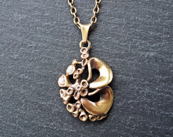 May include: A vintage brass pendant necklace. The pendant features an abstract design with organic shapes and textures. The necklace has a delicate chain and a warm, antique gold finish. The pendant's design includes rounded and textured elements.