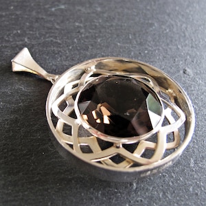 May include: A silver pendant featuring a dark brown gemstone set within a Celtic knot design.