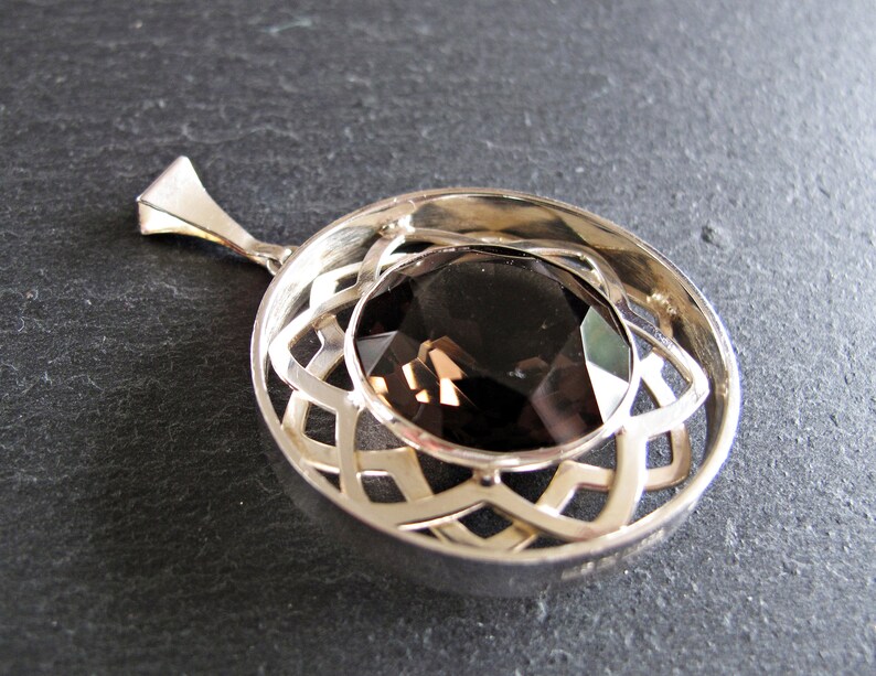 May include: A silver pendant featuring a dark brown gemstone set within a Celtic knot design.