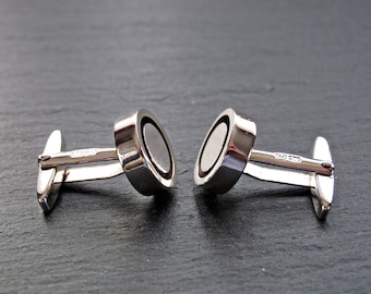 May include: A pair of silver cufflinks with a circular design. Each cufflink has a silver ring around a black center.