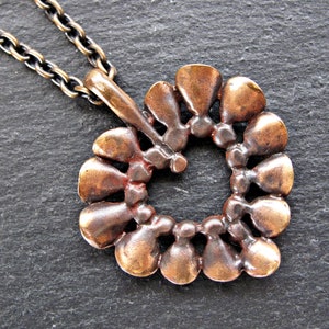 May include: A bronze heart-shaped pendant necklace with a chain. The pendant is made of a series of small, overlapping teardrop shapes.