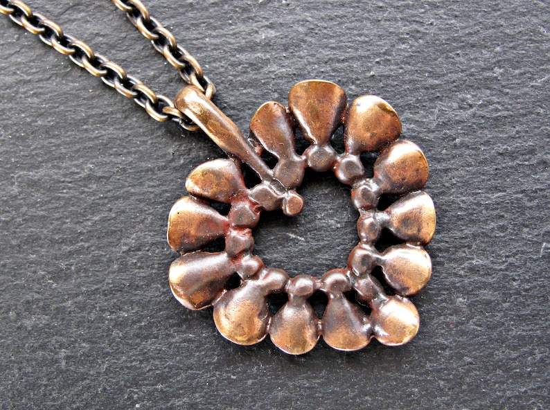 May include: A bronze heart-shaped pendant necklace with a chain. The pendant is made of a series of small, overlapping teardrop shapes.