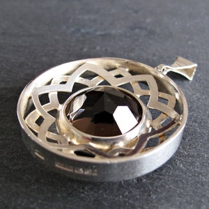 May include: Silver pendant featuring a black gemstone set within a circular, openwork design. The pendant has a bail for attaching to a chain.