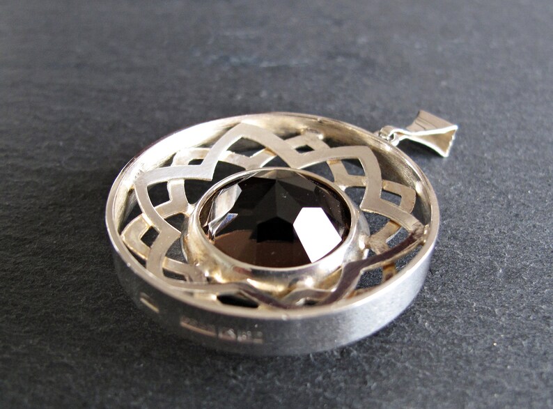 May include: Silver pendant featuring a black gemstone set within a circular, openwork design. The pendant has a bail for attaching to a chain.