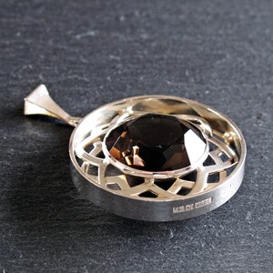 May include: A silver pendant featuring a dark brown gemstone set within a geometric design. The pendant has a bail and is hallmarked "925" on the reverse.