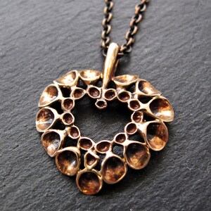 May include: A bronze pendant in the shape of a heart, with a textured design of small, rounded shapes. The pendant is attached to a chain.