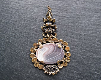 May include: A gold pendant featuring an intricate floral design and a large, oval-shaped agate stone with swirling white and grey patterns.