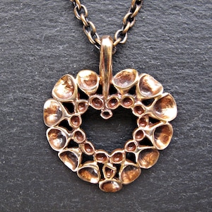 May include: A bronze heart-shaped pendant necklace with a detailed design of small circles and rounded shapes. The pendant is attached to a chain.