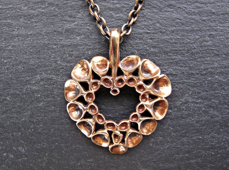 May include: A bronze heart-shaped pendant necklace with a detailed design of small circles and rounded shapes. The pendant is attached to a chain.