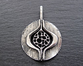 May include: A silver pendant with a circular design featuring a textured outer edge and a geometric, openwork center.