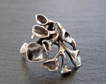 May include: A silver ring featuring a distinctive, organic design reminiscent of a tree branch with numerous offshoots. The ring is crafted from textured metal and has a rustic, handcrafted appearance.