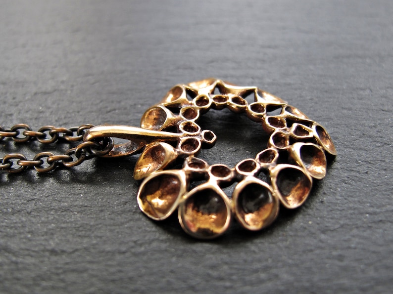 May include: A bronze pendant necklace with a circular design featuring a repeating pattern of small, rounded shapes. The pendant is attached to a chain.