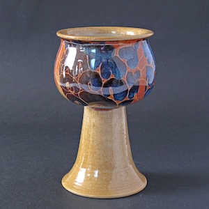 Könnte beinhalten: Ein Keramikkelch mit einem braunen, blauen und orangefarbenen Blumenmuster. Der Kelch hat eine breite, runde Schale und einen hohen, schlanken Stiel.