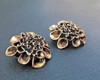 May include: A pair of bronze earrings with a floral design. The earrings are made of a textured metal and have a delicate, intricate design.
