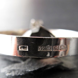 May include: Close-up of a silver ring with a black stone. The ring is hallmarked with "925H" and "A 57".
