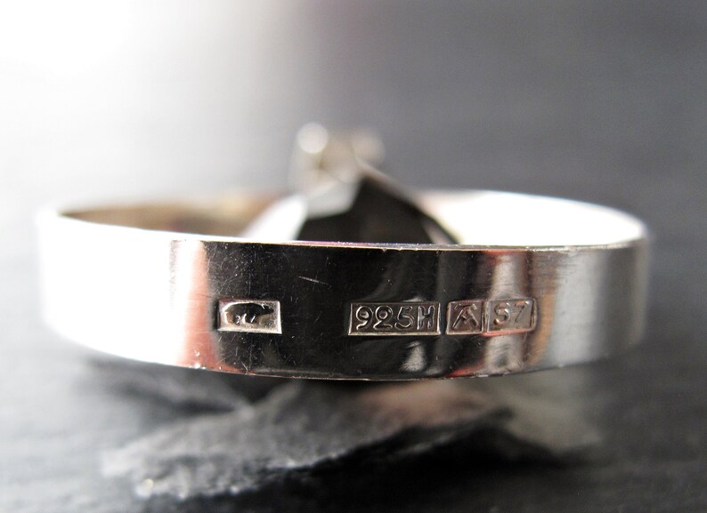 May include: Close-up of a silver ring with a black stone. The ring is hallmarked with "925H" and "A 57".