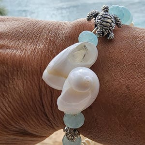 May include: A bracelet with white seashells, light blue beads, and a silver turtle charm. The stretchable band makes it easy to wear. This ocean-themed jewellery is perfect for those who love the beach and coastal style.