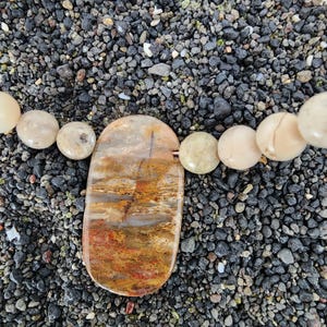 May include: A necklace with a large, oval-shaped agate pendant with brown, orange, and white patterns. The pendant is surrounded by smaller, round, cream-colored beads.