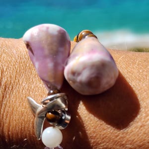 May include: A bracelet with two large, pink and white seashells, a silver dolphin charm, and tiger's eye beads.