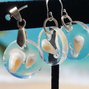 May include: A set of earrings and a pendant featuring clear resin with iridescent seashells inside. The earrings have silver hoops and the pendant has a silver bail.
