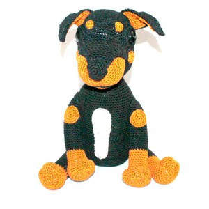 Könnte beinhalten: Ein gehäkeltes schwarzes und oranges Hundespielzeug mit weißen Akzenten. Der Hund sitzt mit gekreuzten Beinen.