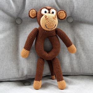 May include: A brown crocheted monkey toy with a ring for a body. The monkey has a smiling face with white eyes and a brown nose.