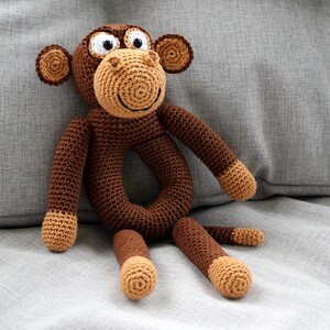 May include: A brown crocheted monkey toy with a ring for a baby to hold. The monkey has white eyes and a brown nose.