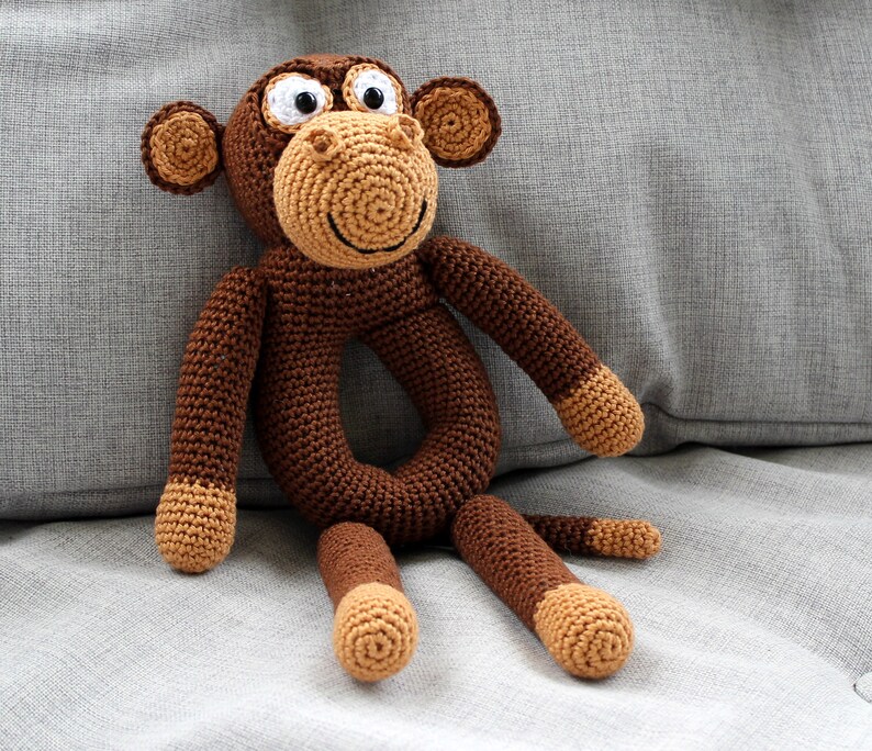 May include: A brown crocheted monkey toy with a ring for a baby to hold. The monkey has white eyes and a brown nose.