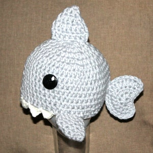 Può includere: Cappello da squalo in crochet grigio con un occhio a bottone nero e denti bianchi.