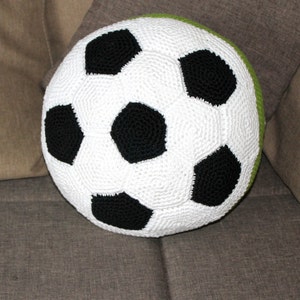 May include: A white and black crocheted soccer ball pillow with a green border.