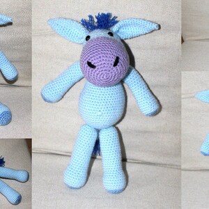 Puede incluir: Un juguete de burro de crochet azul con orejas moradas y una crin azul. El burro está sentado sobre una superficie blanca.