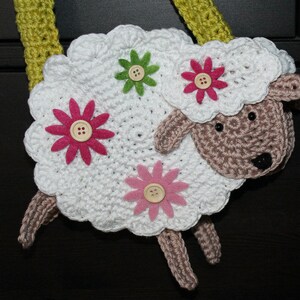 May include: White crocheted sheep with pink and green felt flowers. The sheep has a brown crocheted face and black eyes.