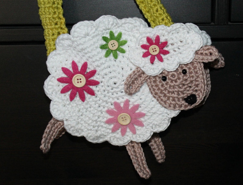 May include: White crocheted sheep with pink and green felt flowers. The sheep has a brown crocheted face and black eyes.
