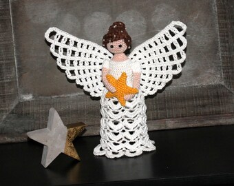 May include: A white crocheted angel figurine holding a yellow crocheted star. The angel has a brown hair and a white dress.