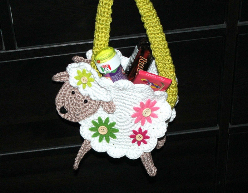 May include: A white crocheted lamb shaped bag with a yellow handle. The bag is filled with candy and other treats.